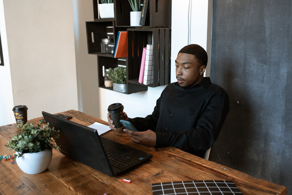 Se Lancer Jeune dans ses Projets : 7 Raisons de ne plus Attendre Black businessman working at a desk with laptop and phone in modern office setting.